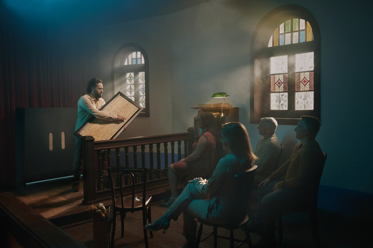 Homem apresentando um grande documento antigo para um grupo de pessoas sentadas em uma sala iluminada por vitrais - Evivva.